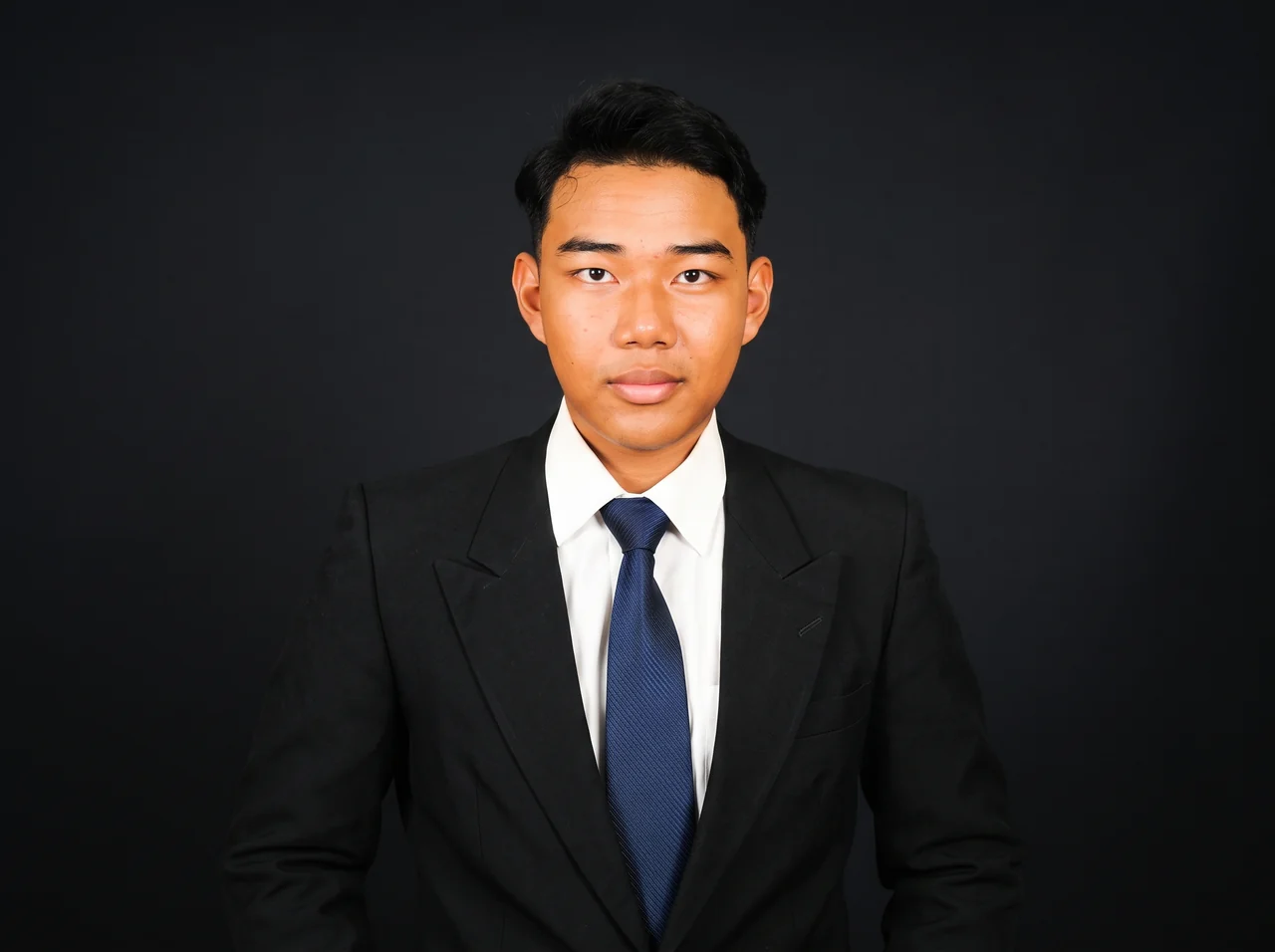 Ikhwanuddin wearing a black suit and navy tie against a dark background